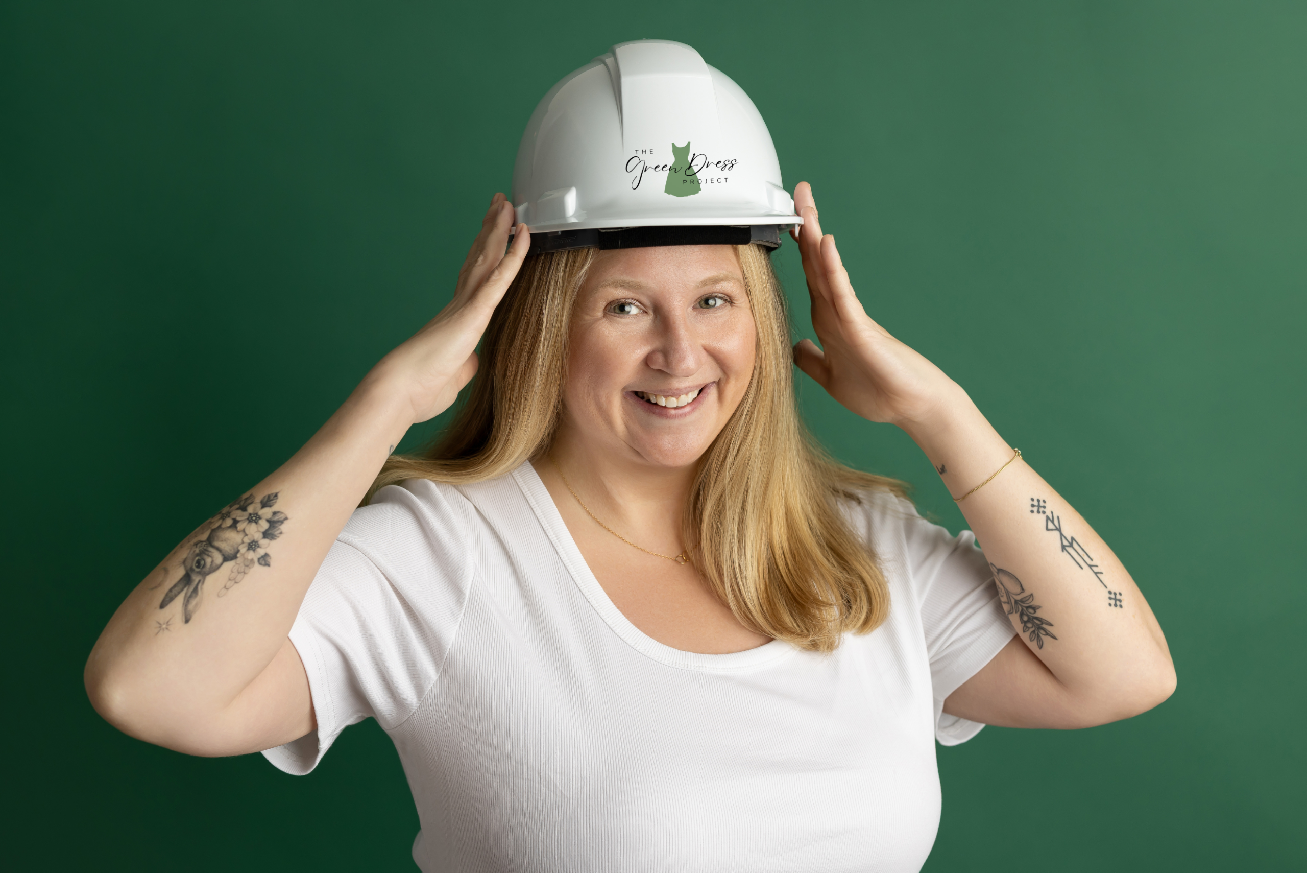 Smiling woman wearing a white safety helmet with a green logo reading 'The Green Dress Project' against a green background.
